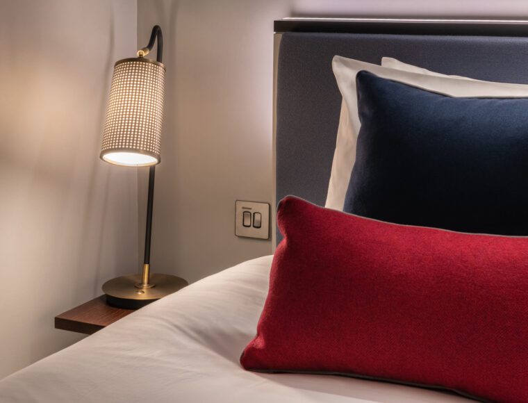 A bedroom's bedside lamp, and double bed with colourful pillows.