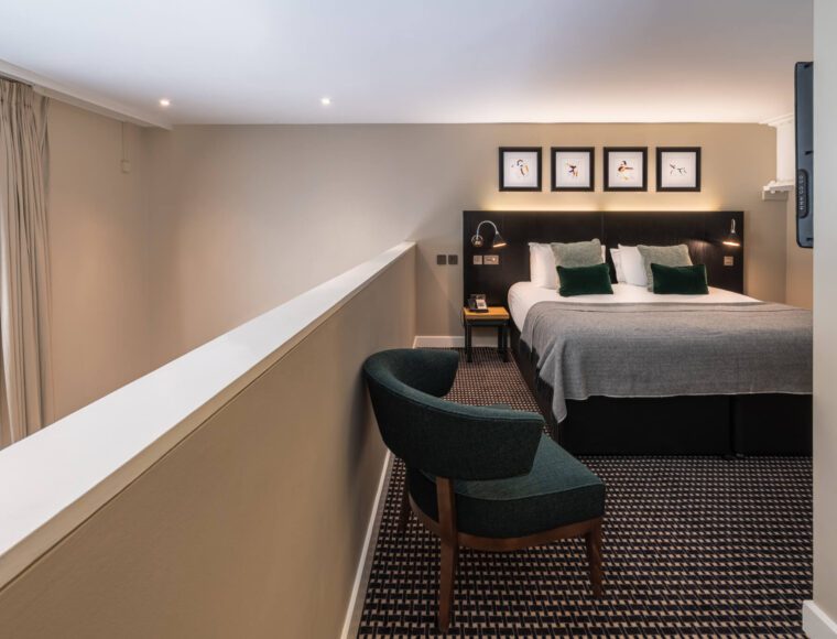 A suite with a double bed, arm chair and bedside table.