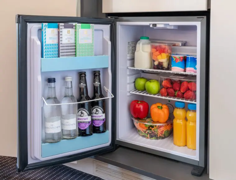 A miniature fridge stocked with beverages, yoghurts and fruit.