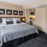 A large suite with a double bed, bedside table and integrated kitchen area.