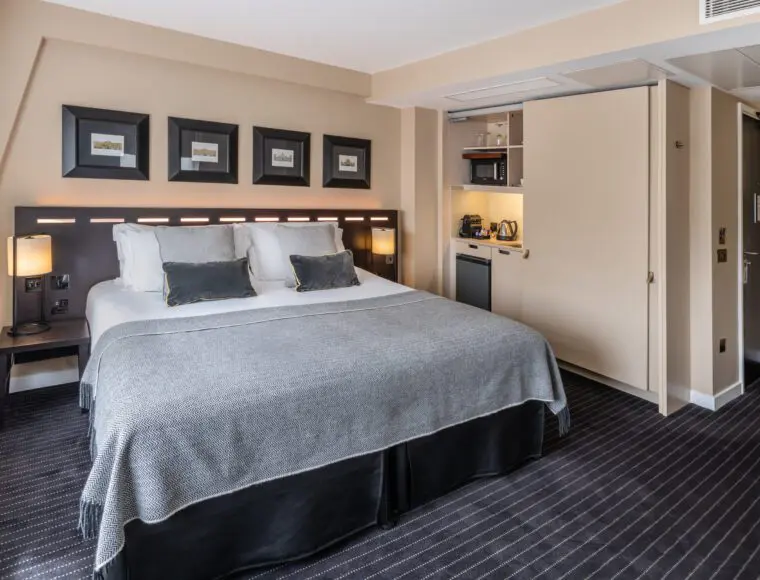 A large suite with a double bed, bedside table and integrated kitchen area.