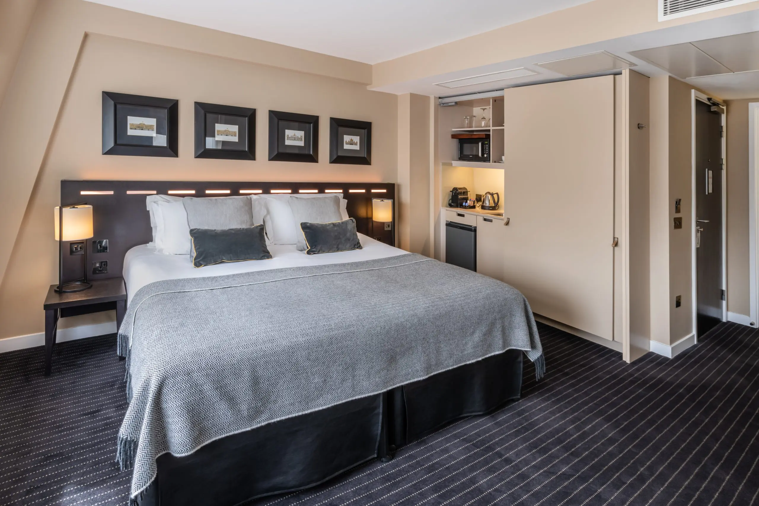 A large suite with a double bed, bedside table and integrated kitchen area.