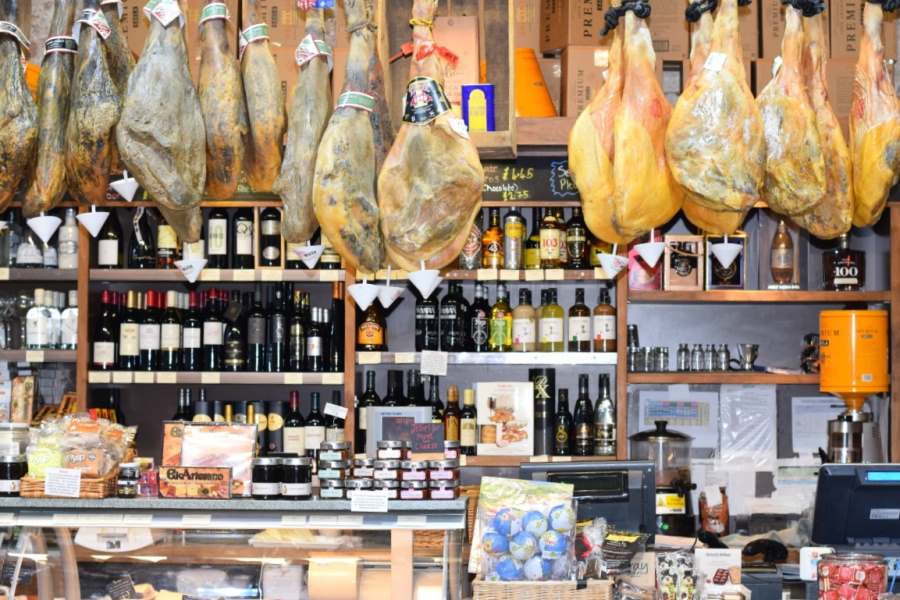 A deli with hanging meats, and wines placed on the shelf.