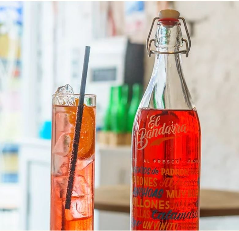 A bottle and glass filled with a red soft drink, served by the Spanish Caravan.