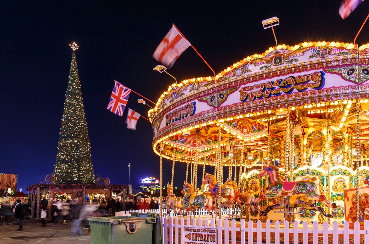 A carousel lit up for the evening, in front of a 40 Foot Christmas Tree at Hyde Park Winter Wonderland,