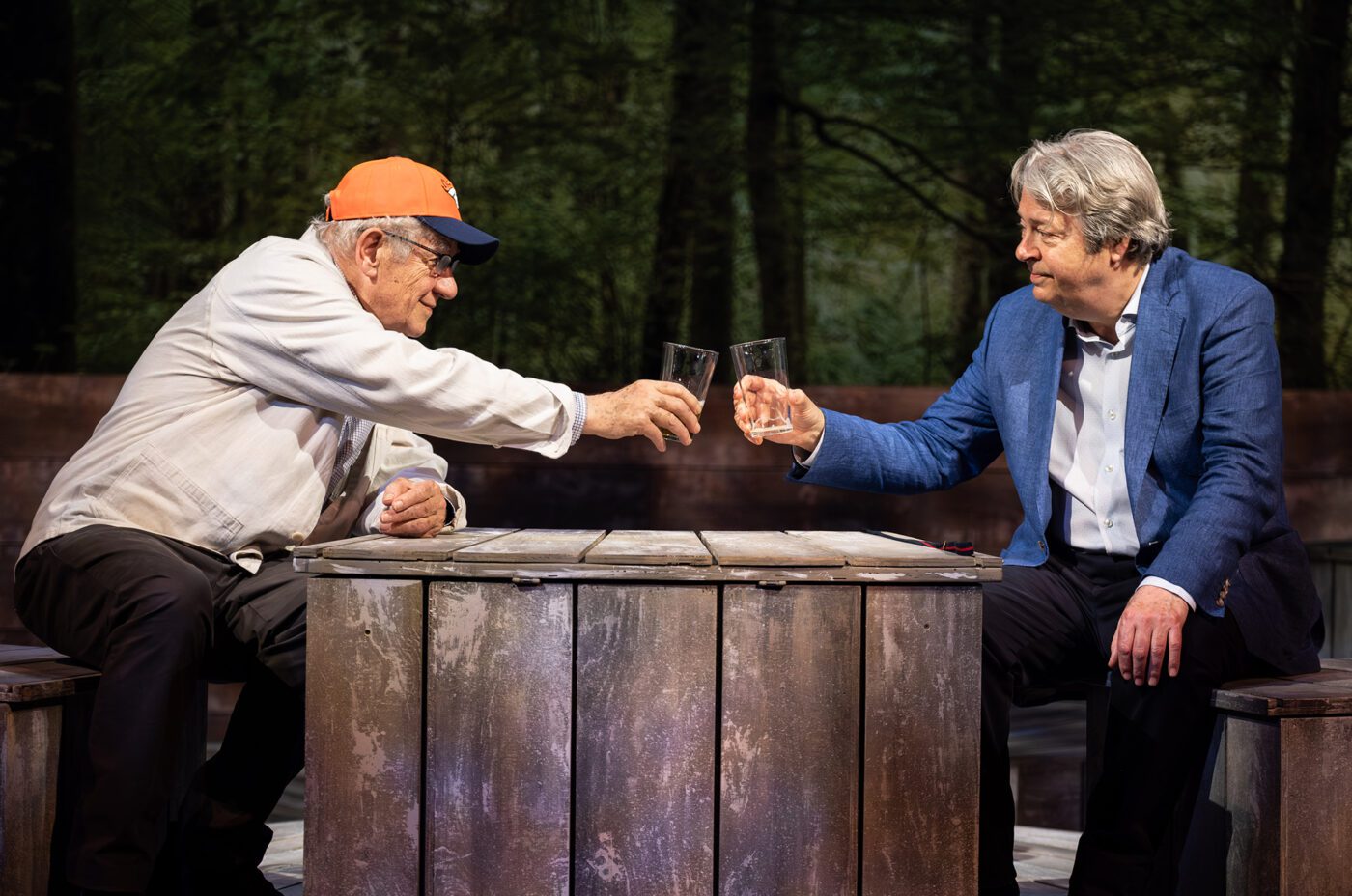 Ian McKellen and Roger Allan on stage toasting glasses.