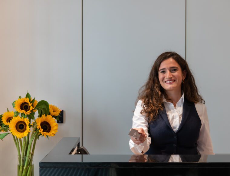 The Resident Team member holding out a room key, next to a vase of sunflowers.