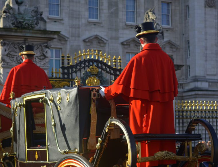 Royal Horse and Carriage approaching the gates of Buckingham Palace in London, with a Windsor Guard stood of the back.