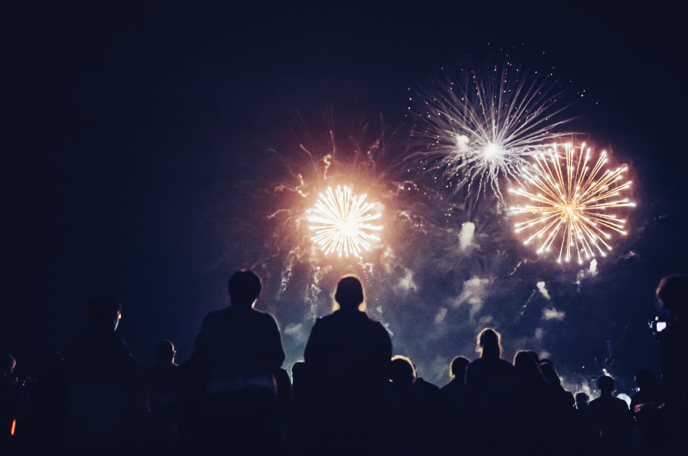 A crowd of people watches colourful fireworks burst in the night sky at the British Musical Fireworks Championship, lighting up the darkness with bright, glowing patterns.